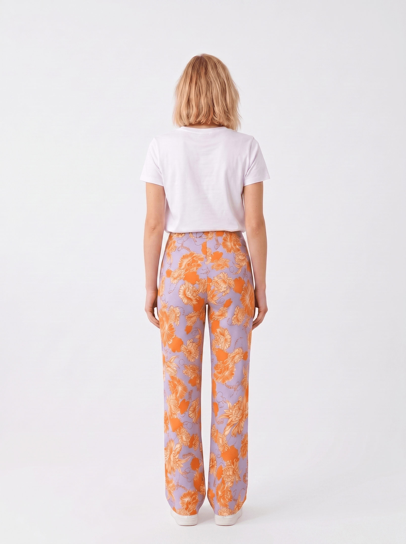 KI generiertes Modell im weißen Studio in der Hose Spino im Print Fleurs von hinten Orange vom Hamburger Modelabel stegmann mode