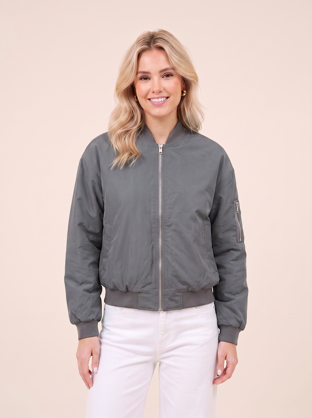 Halbtotale vom KI generiertem Modell in einem hellen Studio in einer Bomberjacke in der Farbe Grau vom Hamburger Modelabel Stegmann Mode
