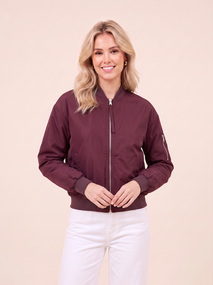 Halbtotale vom KI generiertem Modell in einem hellen Studio in einer Bomberjacke in der Farbe Bordeaux vom Hamburger Modelabel Stegmann Mode