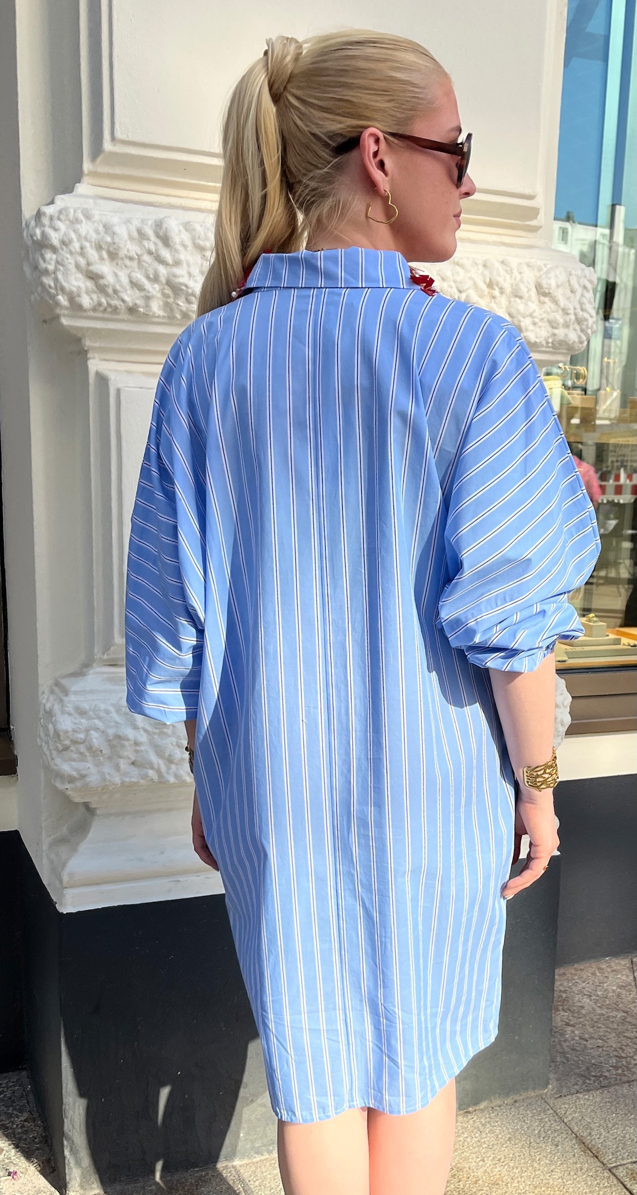 junge Frau im urbanen Umfeld von hinten im Streifenkleid mit Perlenstickerei am Kragen vom Hamburger Modelabel Stegmann Mode